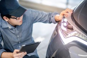 Man in hat examining headlight with tablet in hand