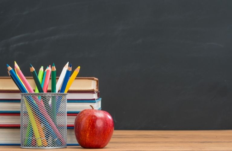 A stack of books, an apple and pencils