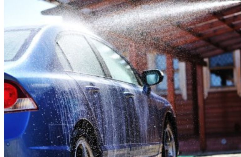 Water splashing over a blue car while cleaning it