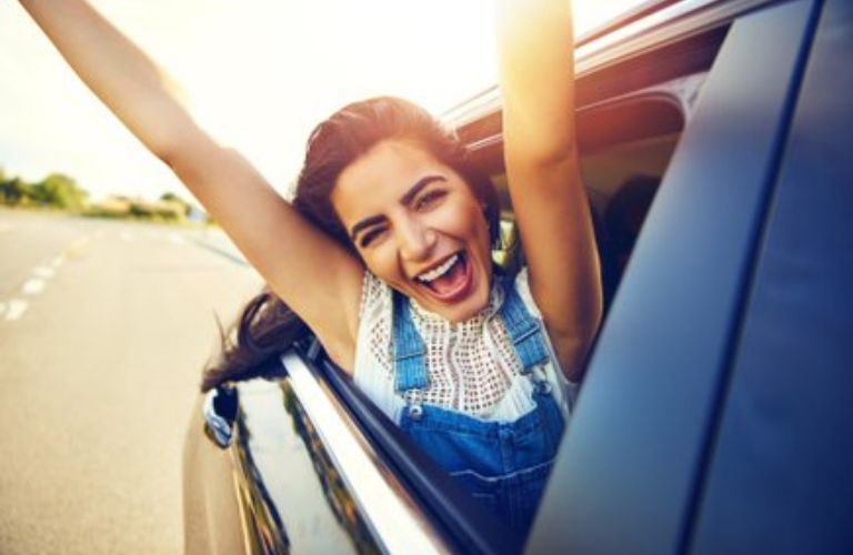 A happy lady looking from the window of a car.