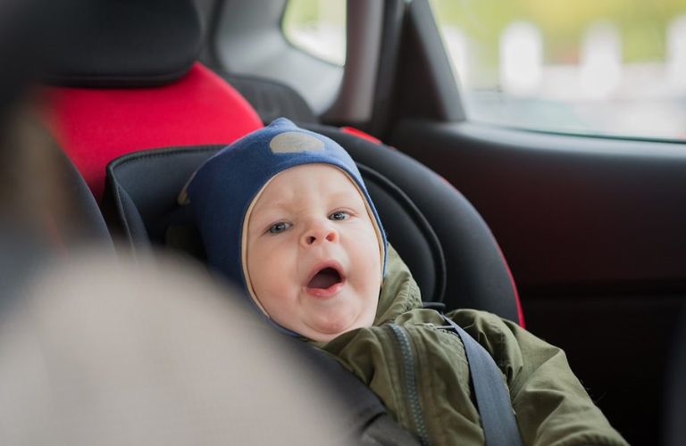 A baby sitting in a car seat is yawning.