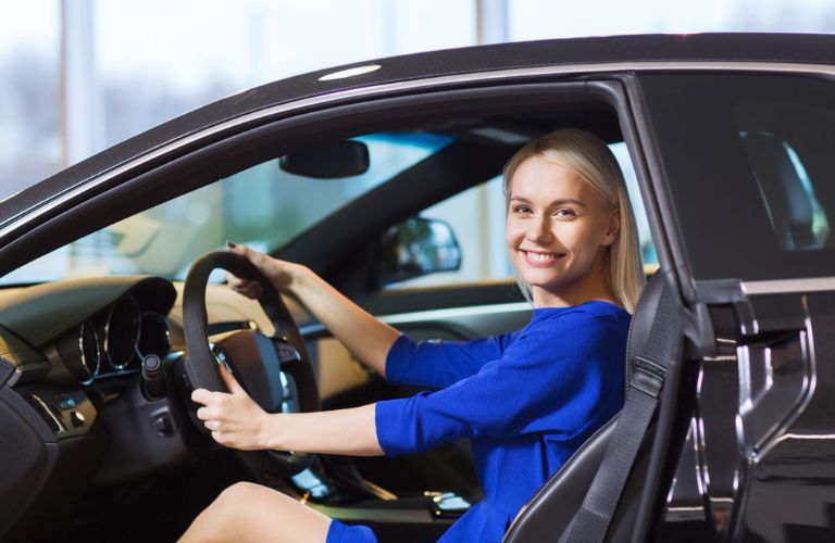 One happy lady in blue dress is sitting in a car with one door open.