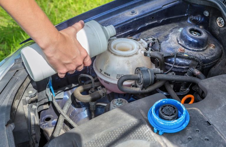 A female hand pouring coolant in the cooling system of a car.