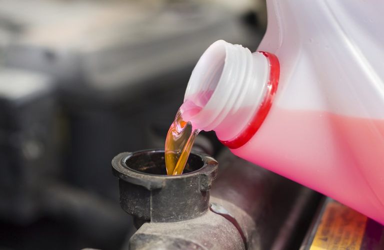 Close up image of coolant being poured from a bottle in the cooling system of a car.